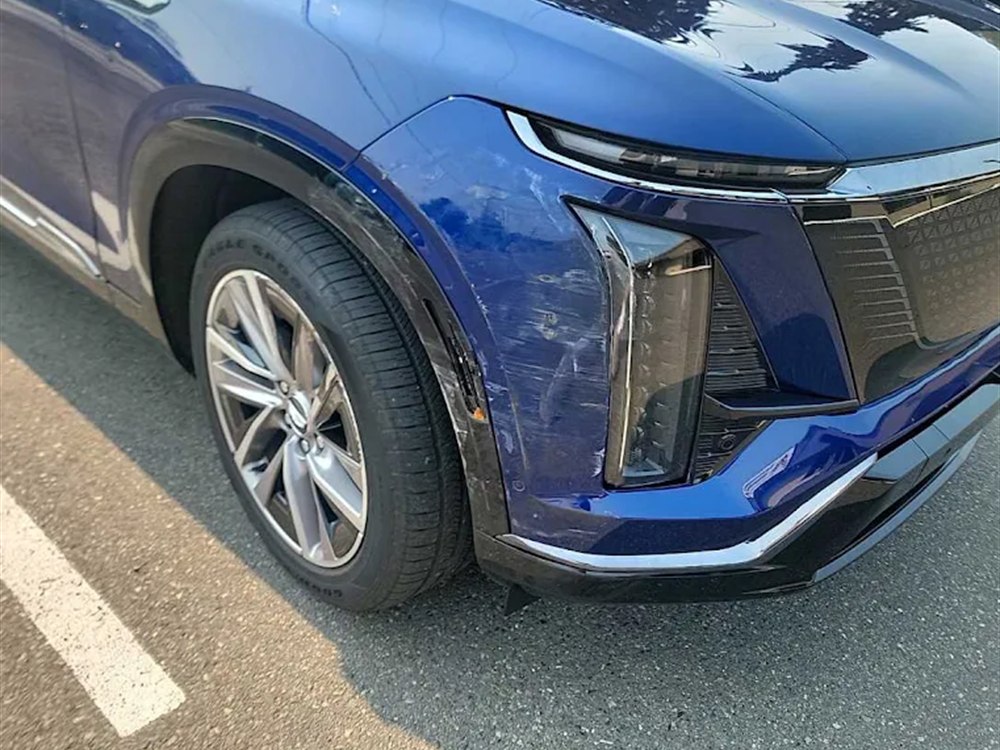Cadillac electric SUV with the front left bumper and fender scraped and creased, before repair