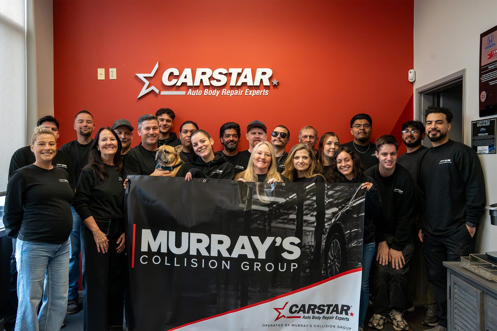 The Murray's CARSTAR Collision team holding a Murray's Collision Group banner in front of the CARSTAR sign at the shop